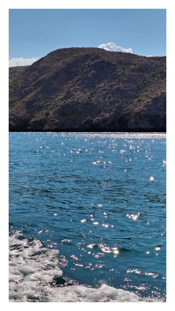 Sunlight glittering on blue water below a rocky hill