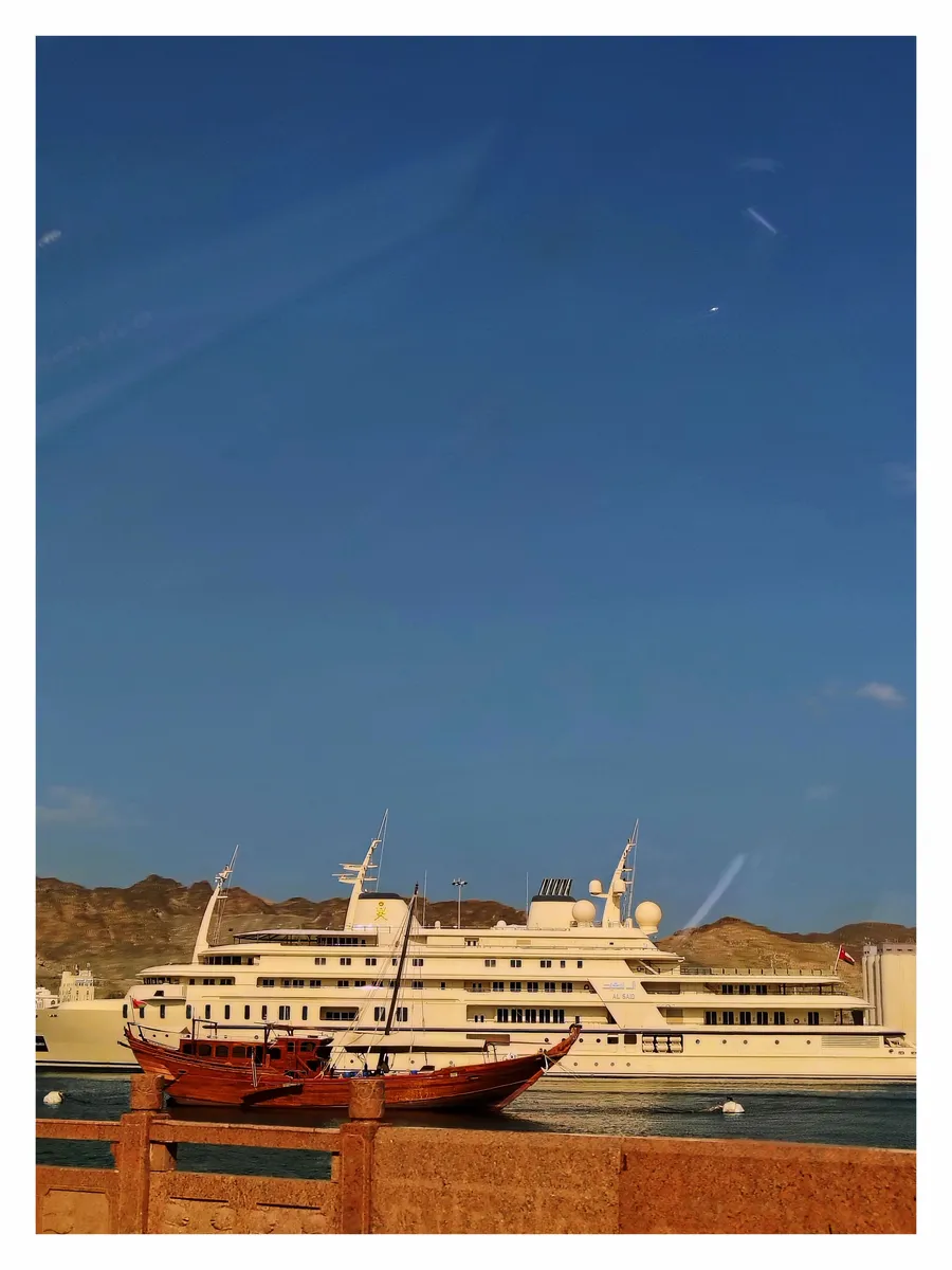 A wooden dhow moored in front of a white royal yacht under a blue sky