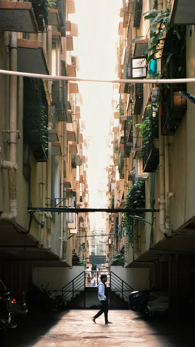 A narrow alley between apartment blocks with one person walking through the light