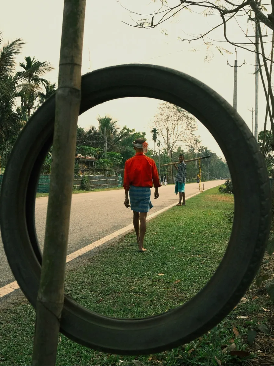 Two men on a village road framed through a hanging tyre