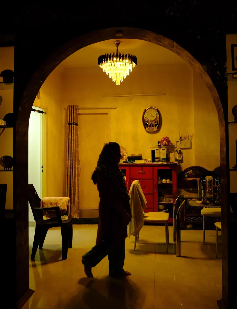 A woman in silhouette walking past an arch into a room lit by a chandelier